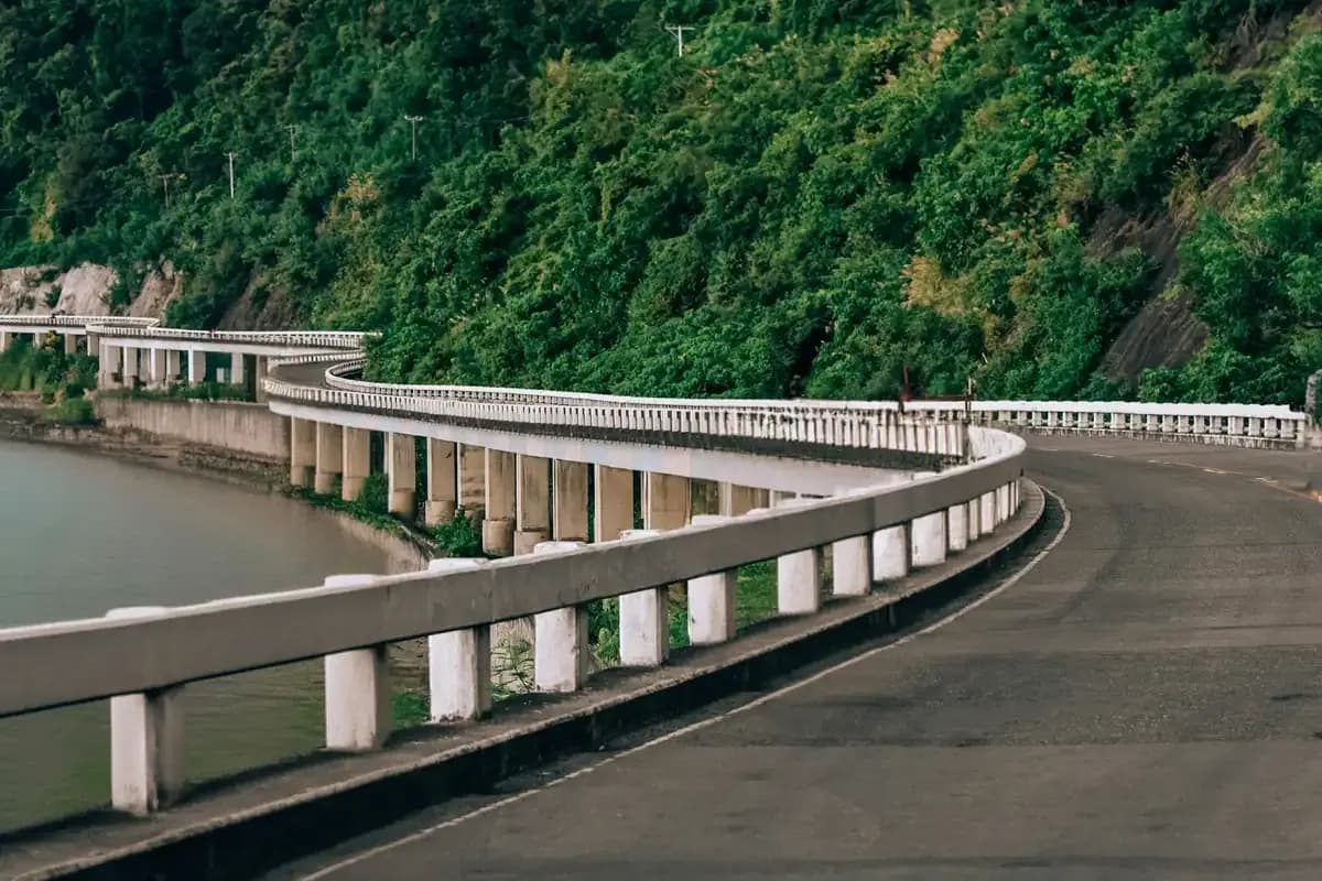 A concrete viaduct curving along a forested coastline