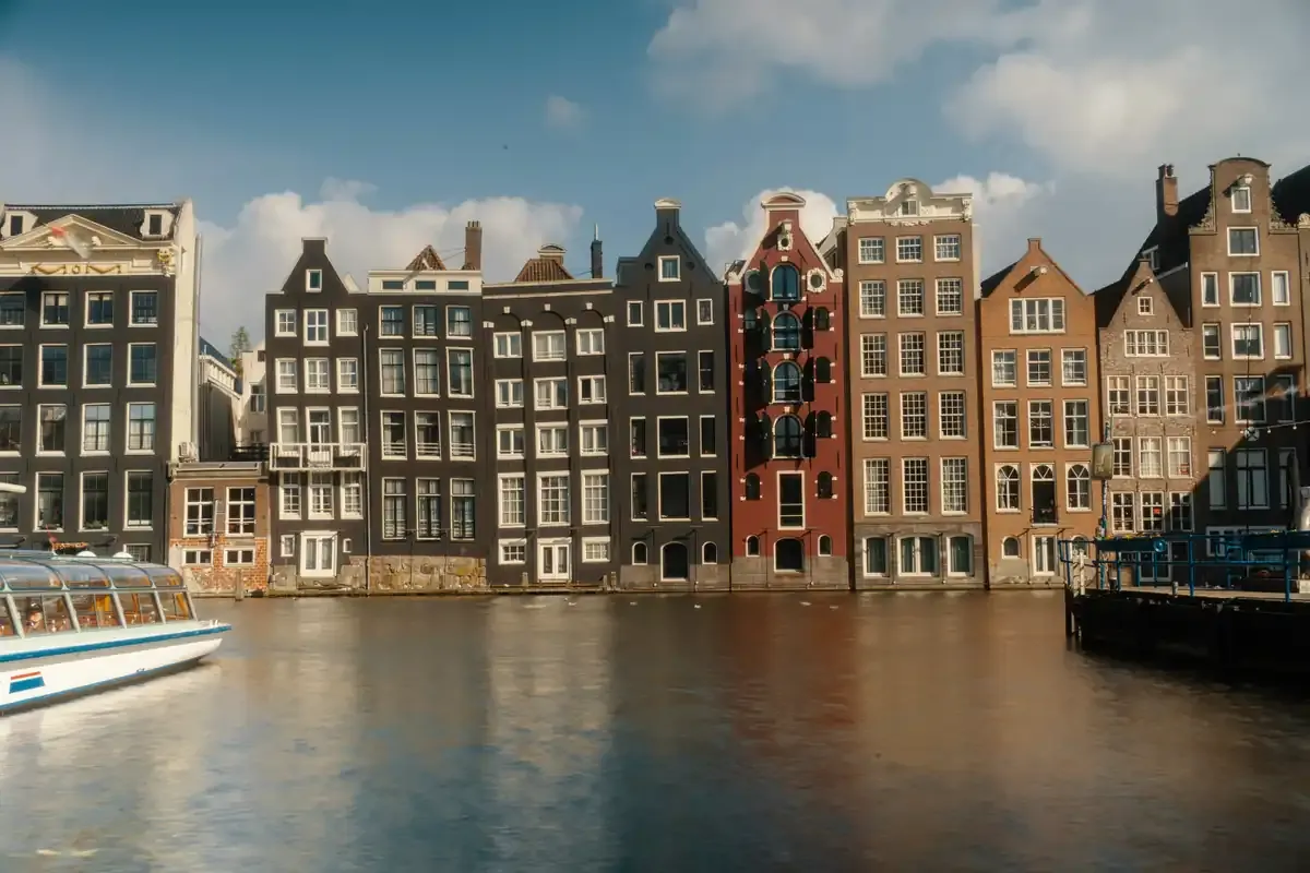 A row of historic gabled houses along a city canal, with a tour boat passing