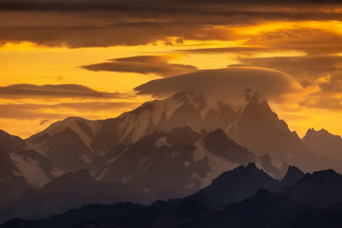 Snow-covered peaks silhouetted against a burning orange sunset